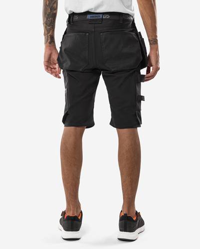 Person, von hinten aufgenommen, trägt schwarze Arbeitsshorts, bei denen Taschen und Werkzeugschlaufen sichtbar sind; steht vor einem schlichten weißen Hintergrund.