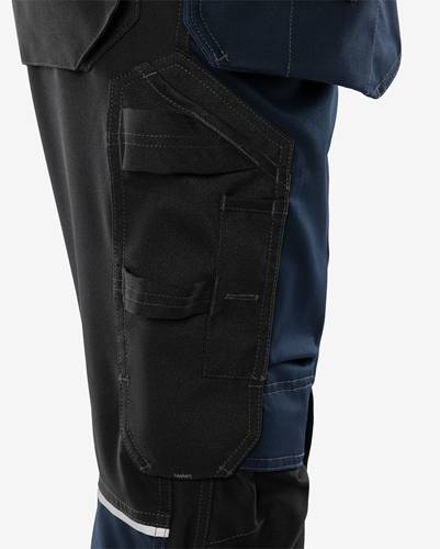 Eine Nahaufnahme einer Person, die dunkle Arbeitshosen mit mehreren Taschen trägt. Die Hosen haben sichtbare Nähte und eine kontrastierende Tasche.