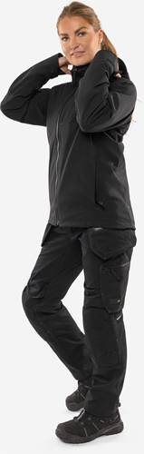 Eine Person trägt eine dunkel gefärbte taktische Kleidung, einschließlich einer Jacke und Hose, und steht vor einem neutralen Hintergrund.