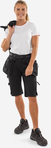 Eine Person, die schwarze Arbeitsshorts mit mehreren Taschen und Schlaufen trägt, vor einem einfarbigen Hintergrund stehend.