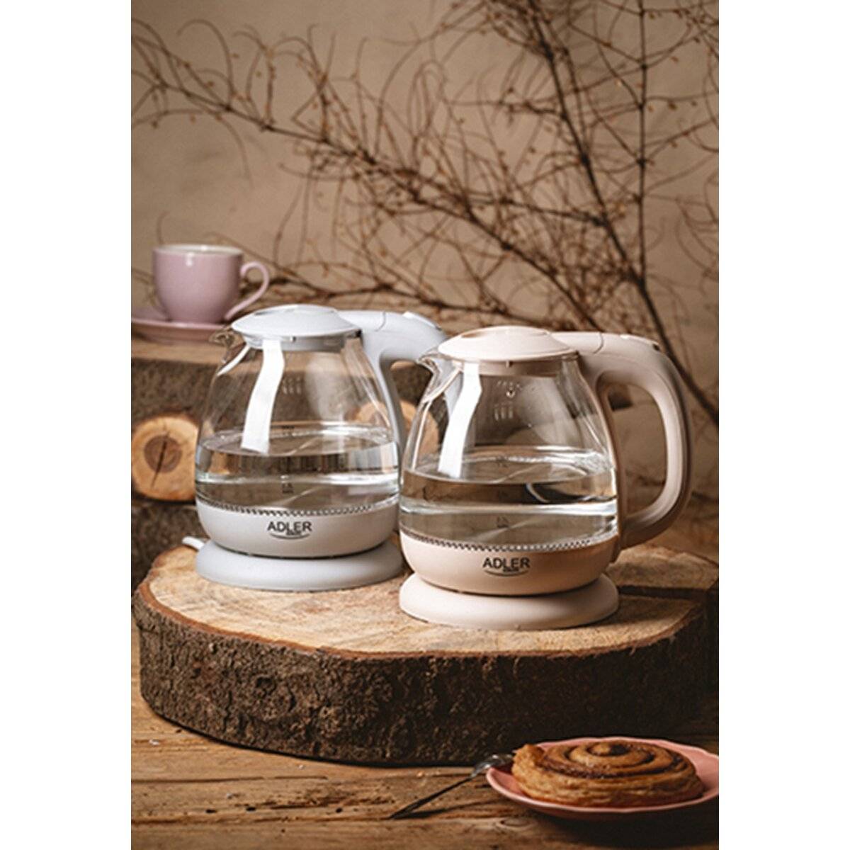 Zwei klare Glaskesselgefüllt mit Wasser stehen auf geschnittenen Holzblöcken. Eine warme Szene mit einem Gebäck und einem Baumzweig im Hintergrund.