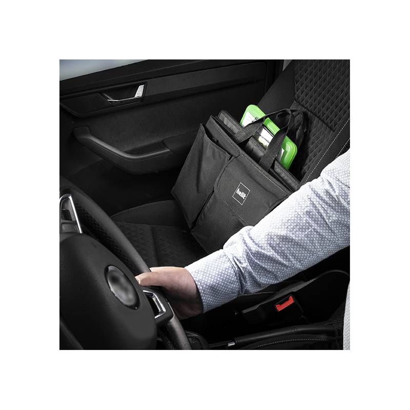 Eine Person in einem Auto hält ein Lenkrad, während eine schwarze Tasche mit einem grünen Ordner auf dem Beifahrersitz liegt.