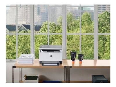 Ein Drucker auf einem Bürotisch neben einem großen Fenster mit Blick auf die Stadtlandschaft und grüne Bäume draußen.