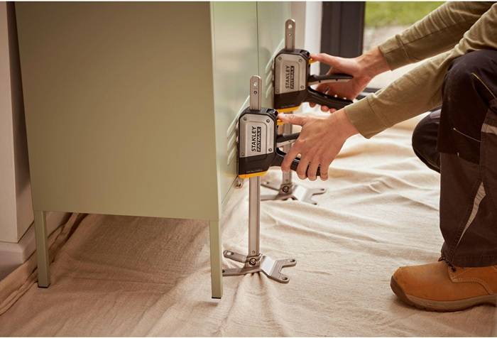 Eine Person, die Stanley-Handklemmen verwendet, um einen Schrank über einer Schutzplane zu befestigen und eine präzise Schrankinstallation zu demonstrieren.
