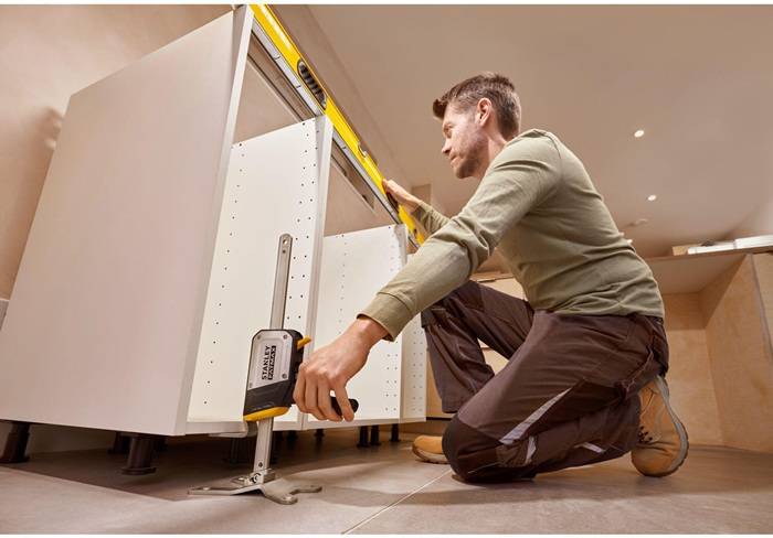 Eine Person, die ein Wasserwaage-Werkzeug verwendet, um Küchenschränke auszurichten und sicherzustellen, dass sie gerade und korrekt bei einer Hausrenovierung installiert sind.