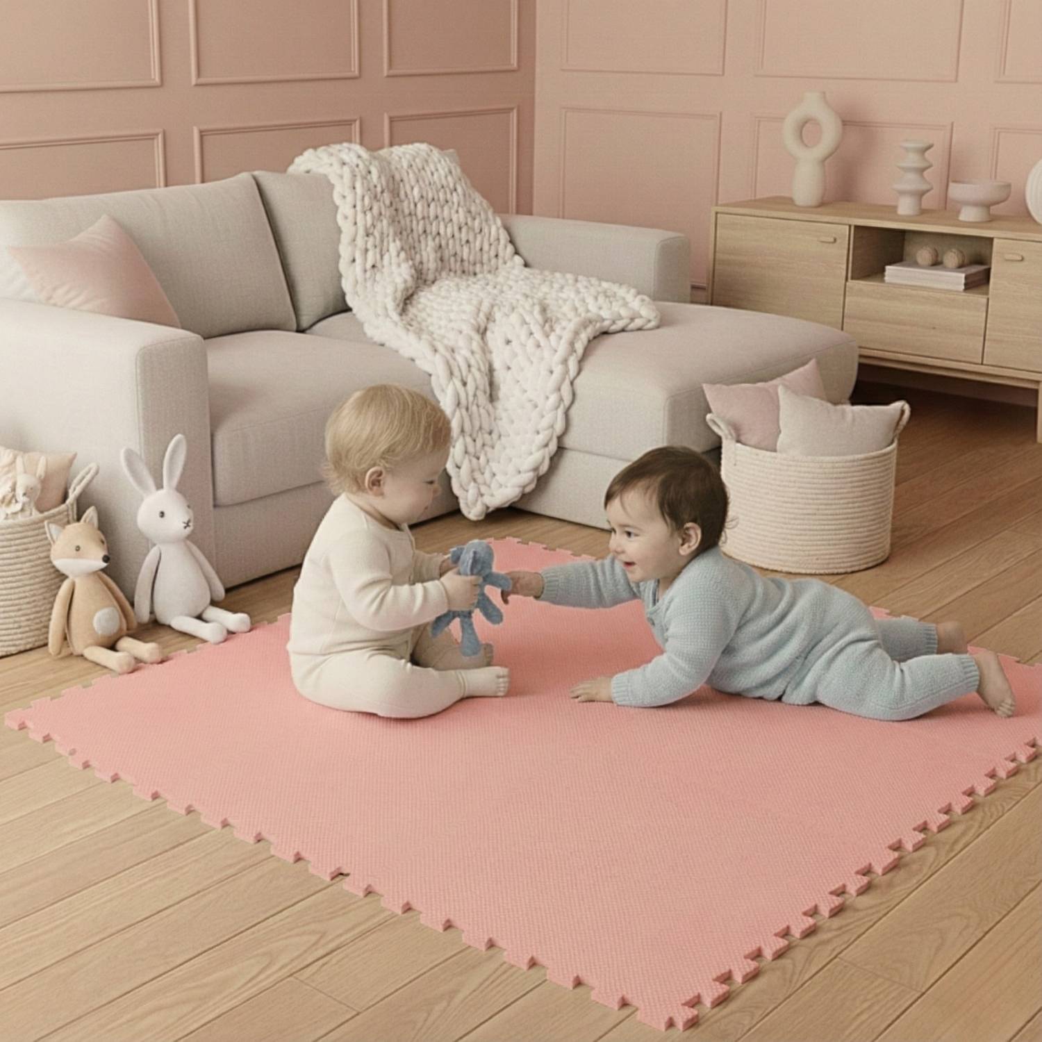 Zwei kleine Kinder spielen auf einer weichen rosa Matte in einem gemütlichen Wohnzimmer mit pastellfarbener Einrichtung. Plüschtiere und eine Decke befinden sich in der Nähe.