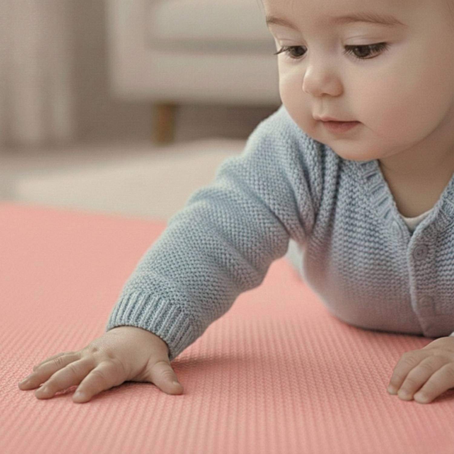 Ein Baby in einem weichen blauen Pullover krabbelt auf einer rosa Matte und blickt neugierig nach vorn. Der Hintergrund ist ein sanft unscharf verwischter Raum.