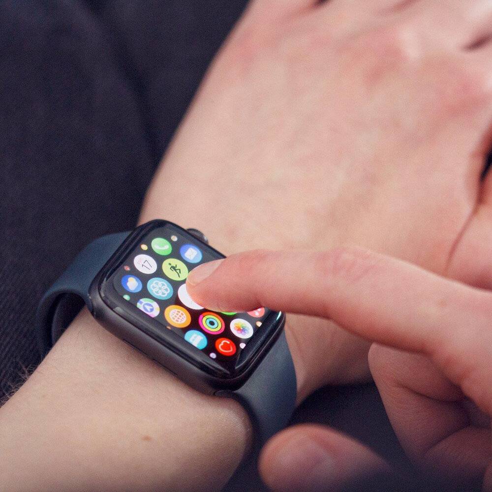 Eine Person interagiert mit einer Smartwatch, die verschiedene farbenfrohe App-Symbole anzeigt, was auf die Nutzung von Technologie für Bequemlichkeit oder Multitasking hindeutet.