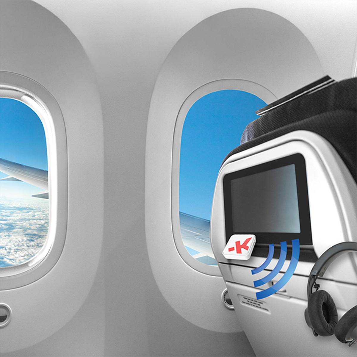 Innenansicht eines Flugzeugs mit zwei Fenstern, blauem Himmel und Wolken, einem Sitzlehnen-Bildschirm und daneben liegenden Kopfhörern.