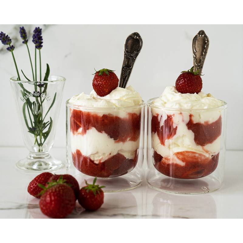 Zwei Glasbecher gefüllt mit geschichteten Erdbeeren und Sahne, gekrönt von ganzen Erdbeeren und Löffeln, neben einem Glas mit Lavendel.