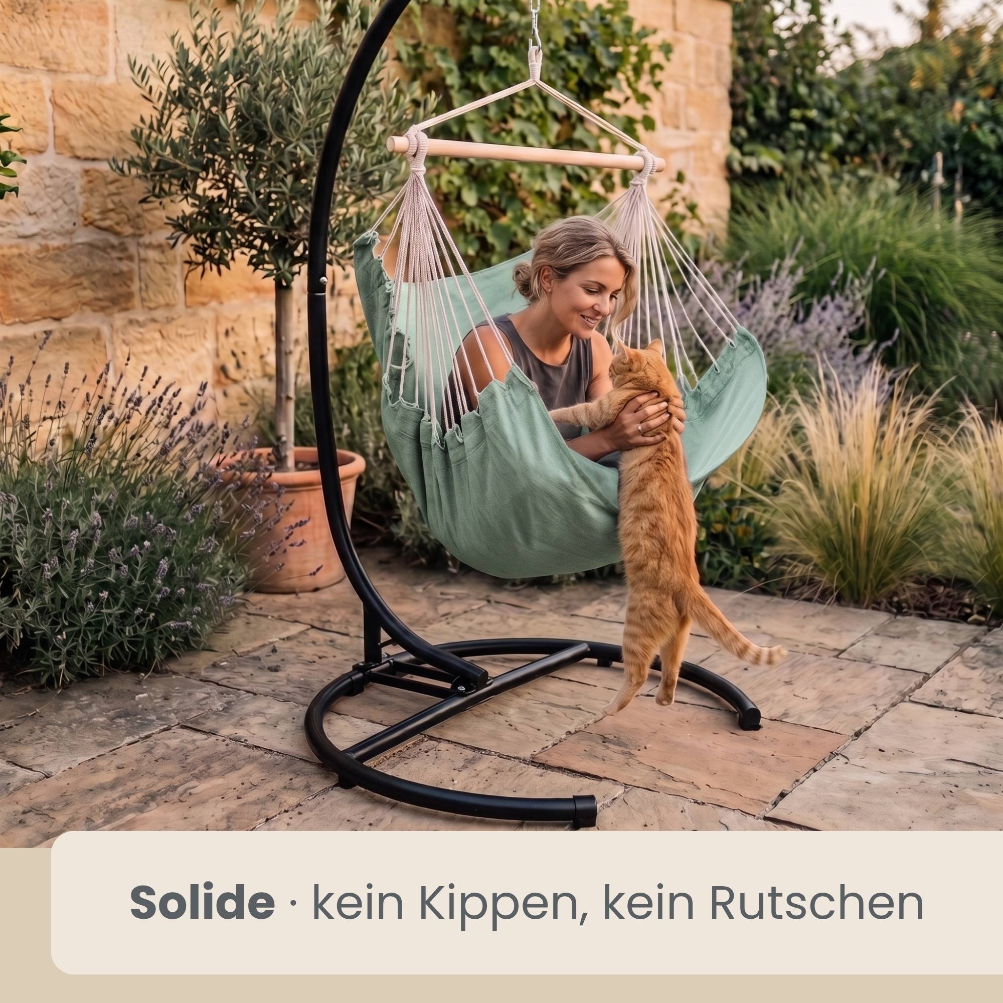 Frau in einem hängenden Hängesessel, die eine orange Katze auf einer Gartenterrasse anlächelt; Text lautet „Solide · kein Kippen, kein Rutschen