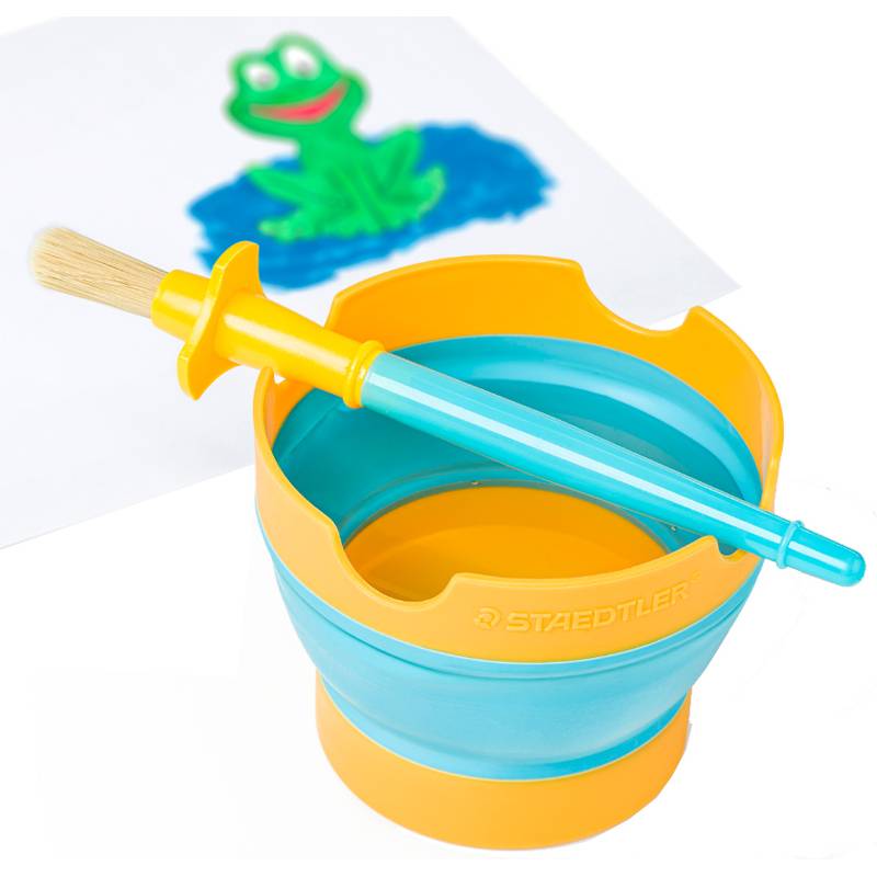 Eine zusammenklappbare Wassertasse mit einem blauen Pinsel, der oben darauf liegt, neben einer Kinderzeichnung eines grünen Frosches auf weißem Papier.