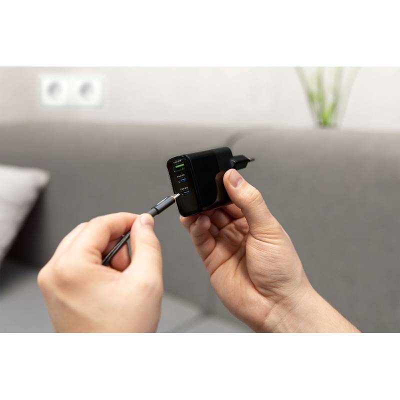 Eine Person steckt ein Kabel in ein schwarzes Wandladegerät mit mehreren USB-Anschlüssen, aufgenommen in Innenräumen.