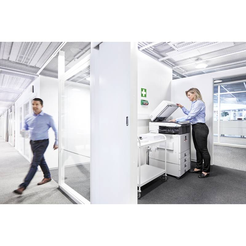 Ein Büroflur mit einer Frau, die einen Kopierer benutzt, und einem Mann, der vorbeigeht, beide in Geschäftskleidung. Moderner und heller Arbeitsbereich.