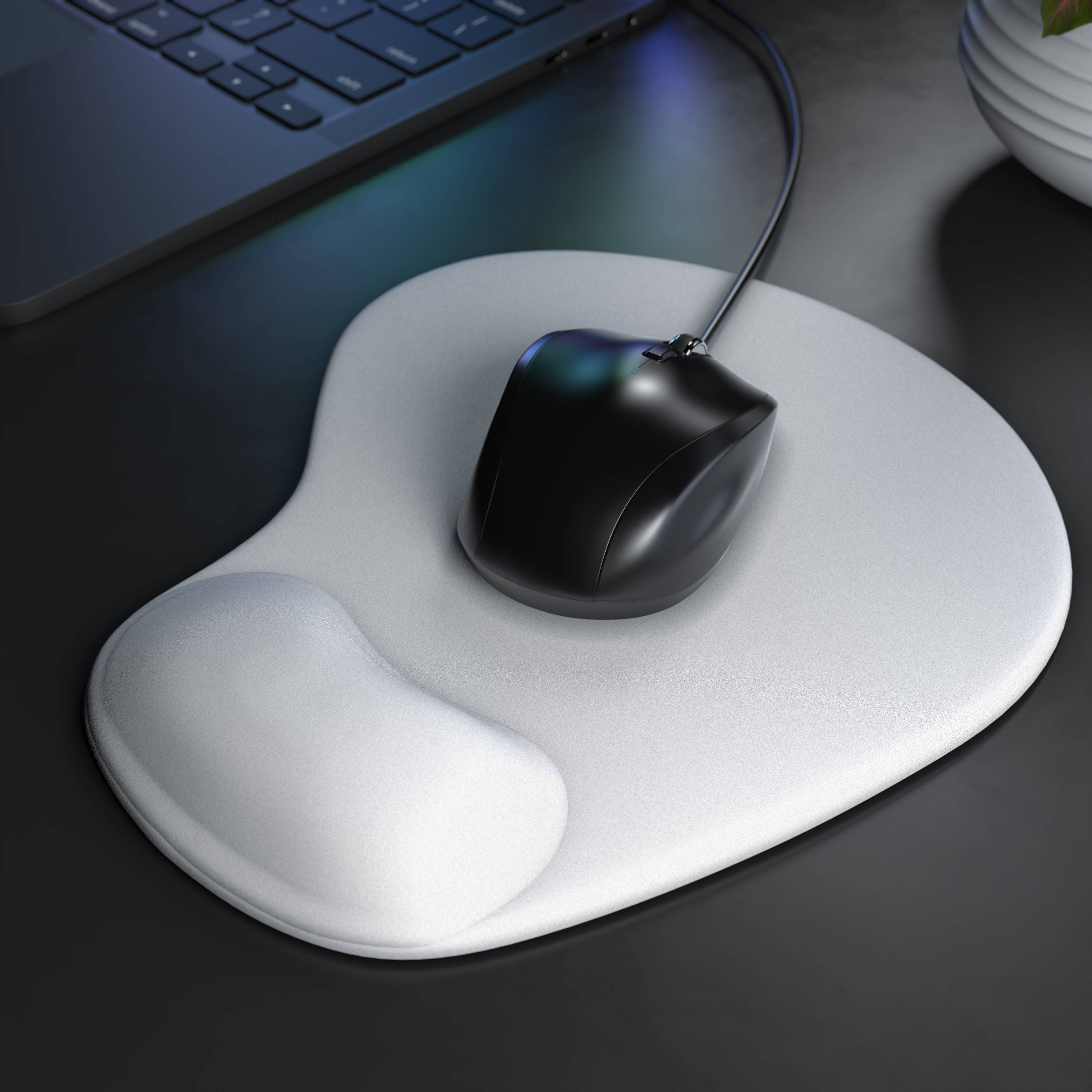 Schwarze schnurgebundene Computermaus auf einem weißen ergonomischen Mousepad neben einer Tastatur auf einem dunklen Schreibtisch.