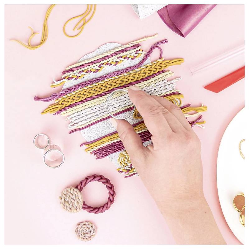 Eine Hand hält eine runde rosa Garnspule und wählt aus verschiedenfarbigen Garnen für ein Handarbeitsvorhaben. Scheren, Ringe und rosa Stoff befinden sich in der Nähe.