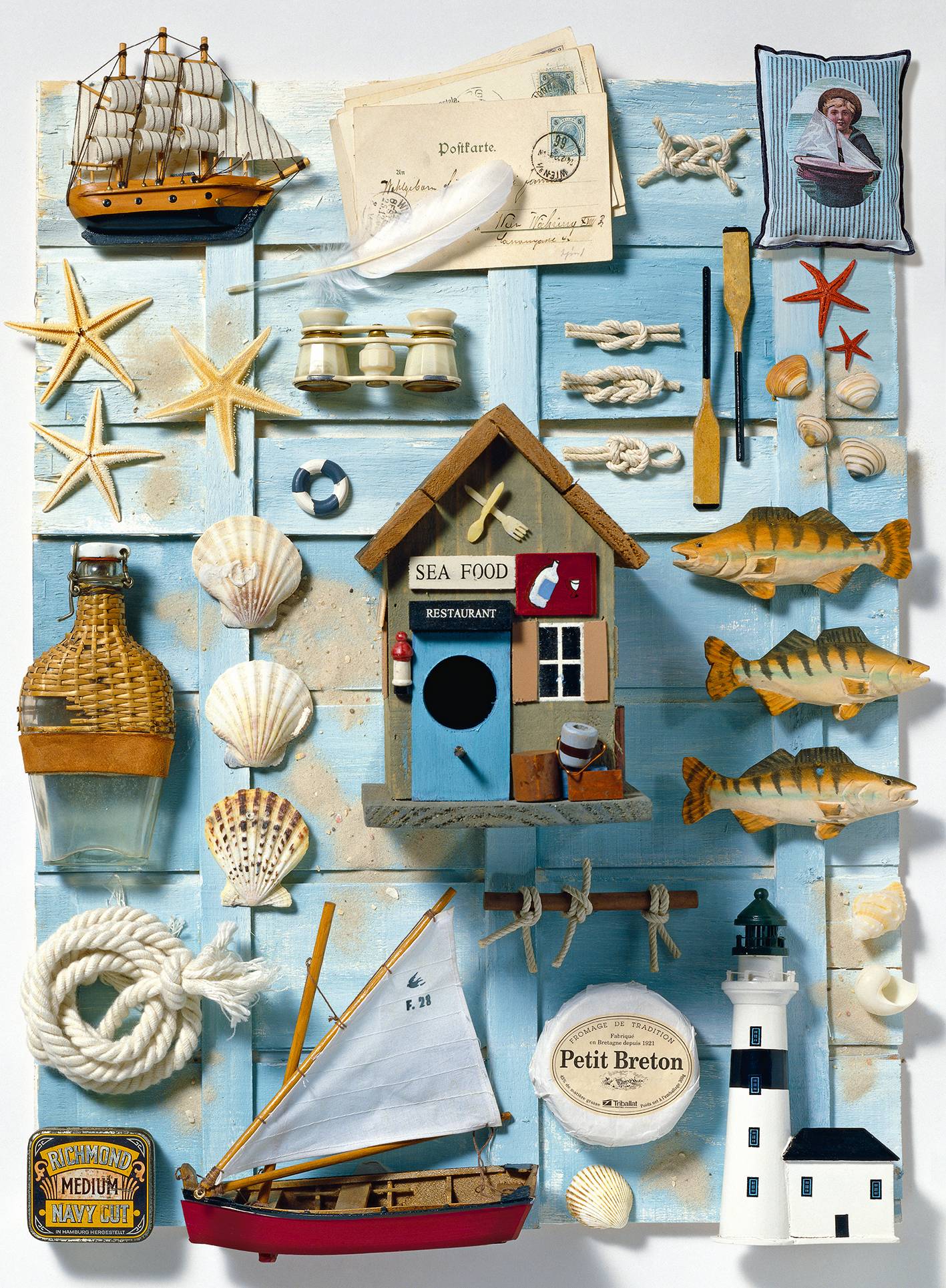 Eine nautische Collage aus Meeresdekor: Modellsegelboote, Leuchtturm, Muscheln, Seesterne, Seil, Fische und ein 