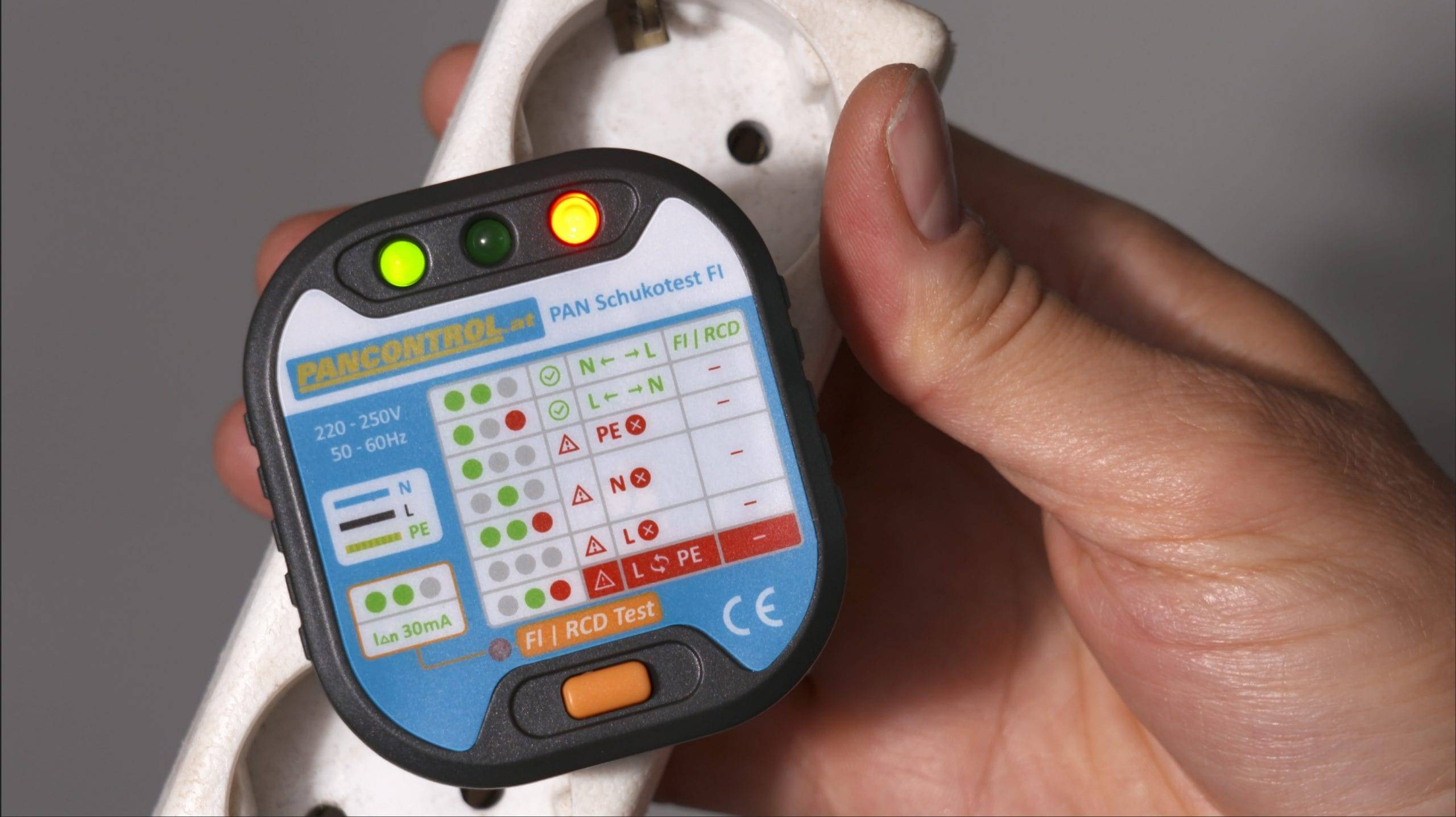 Eine Hand hält einen Steckdosenprüfer mit Leuchten, die Testergebnisse für FI-Schalter und Schutzleiter anzeigen und auf mögliche elektrische Sicherheitsprobleme hinweisen.