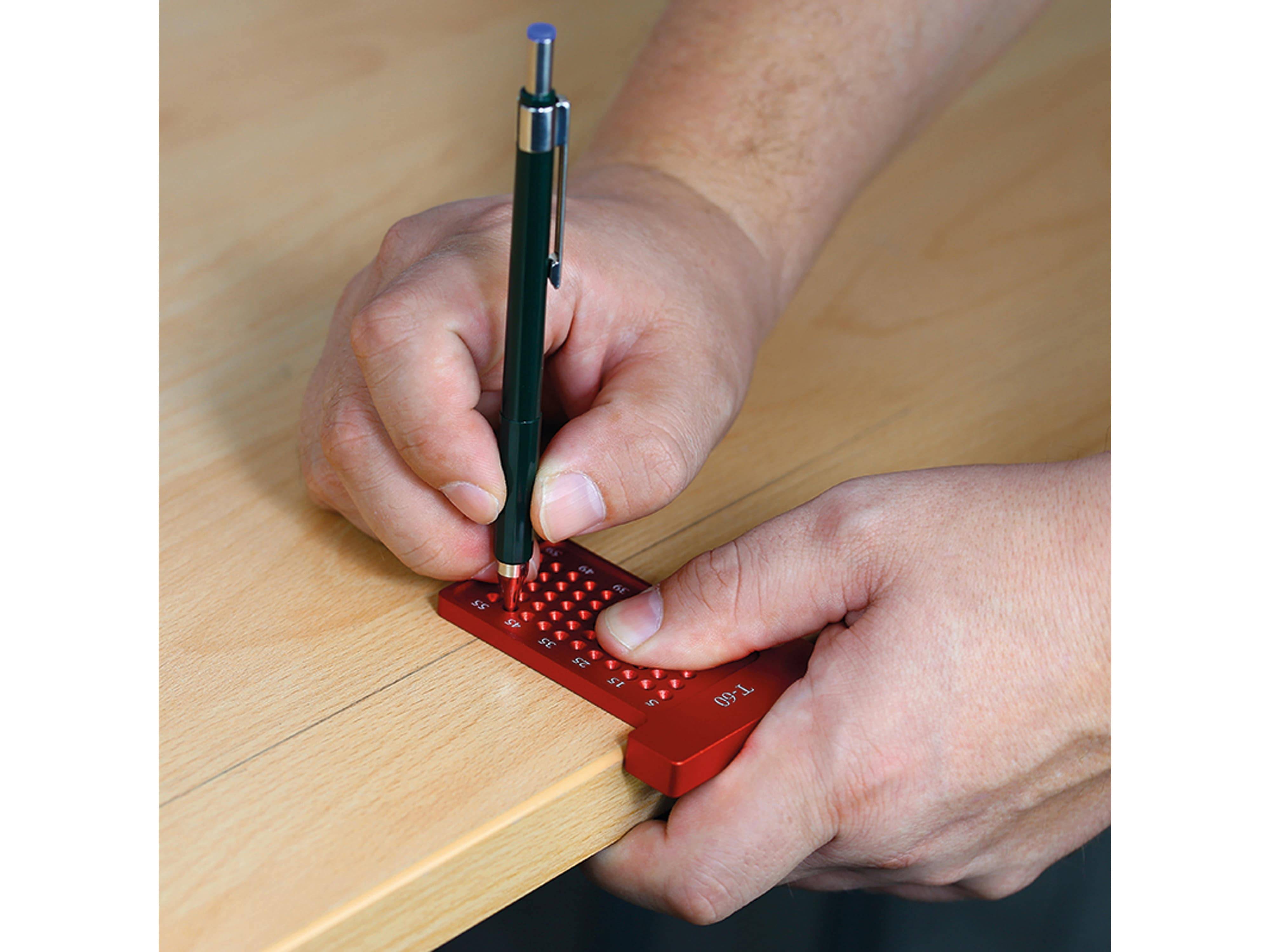 Eine Person, die einen roten Taschenrechner mit Tastfunktion und einen Stift auf einem Schreibtisch verwendet, was zugängliche Hilfsmittel für sehbehinderte Personen verdeutlicht.