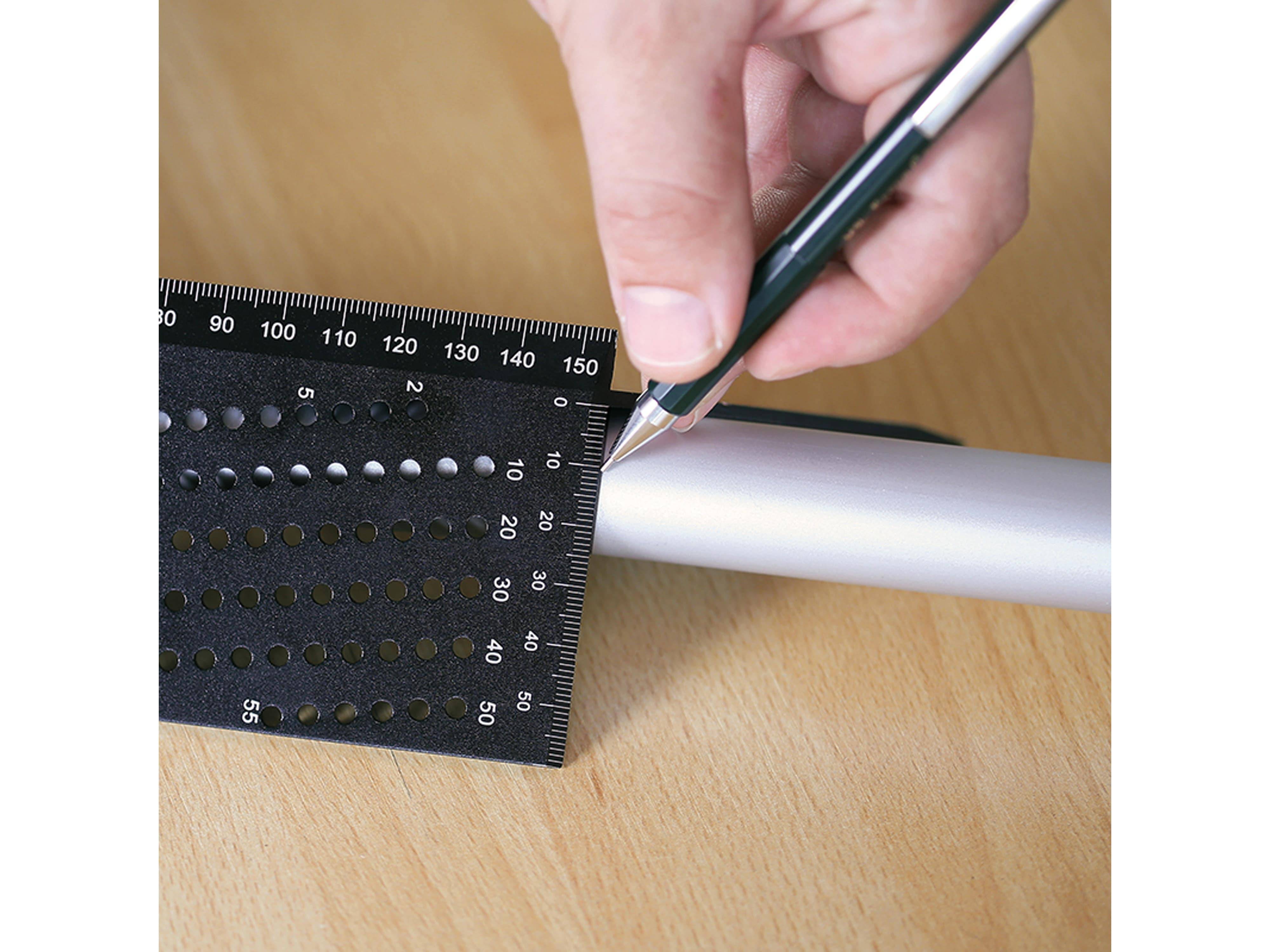 Eine Hand hält einen Stift neben einem Lineal mit Löchern und Markierungen, das zur präzisen Markierung auf einem Metallstab verwendet wird, der auf einer Holzoberfläche platziert ist.