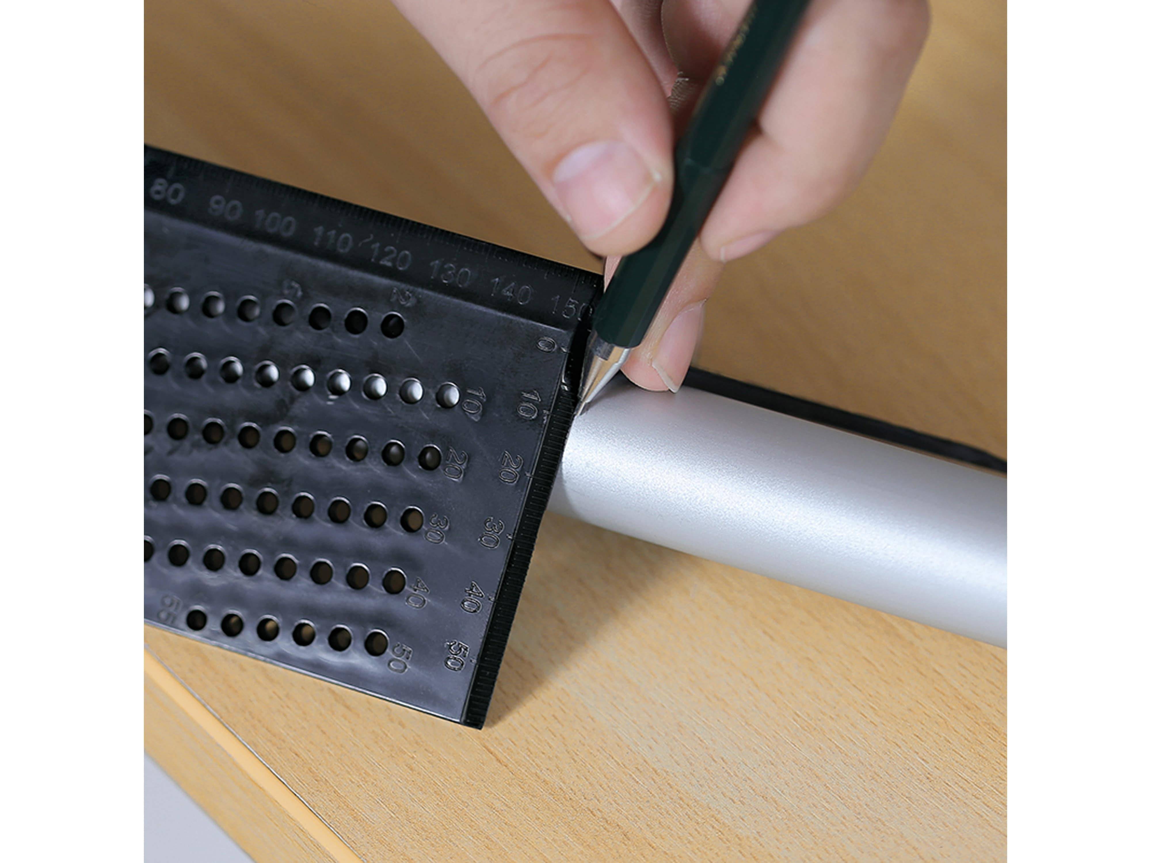 Eine Hand benutzt ein grünes Universalmesser, um weißes Papier entlang eines Metalllineals mit schwarzen Markierungen und Perforierungen zu schneiden. Die Oberfläche ist aus Holz.