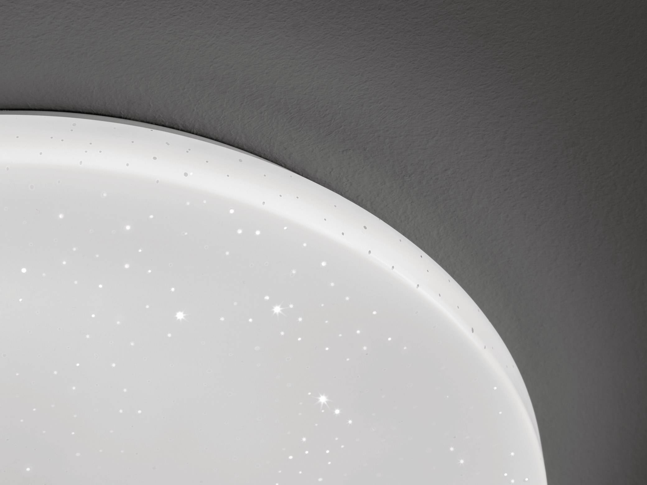 Eine weiße Deckenleuchte mit winzigen sternenähnlichen Mustern, die ein weiches, stimmungsvolles Licht in einem dunklen Raum erzeugt.