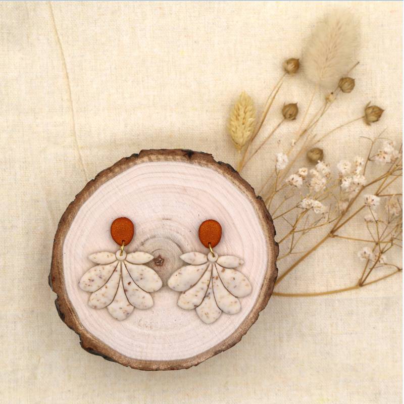 Ein Paar Ohrringe auf einer runden Holzscheibe mit getrockneten Blumen im Hintergrund.