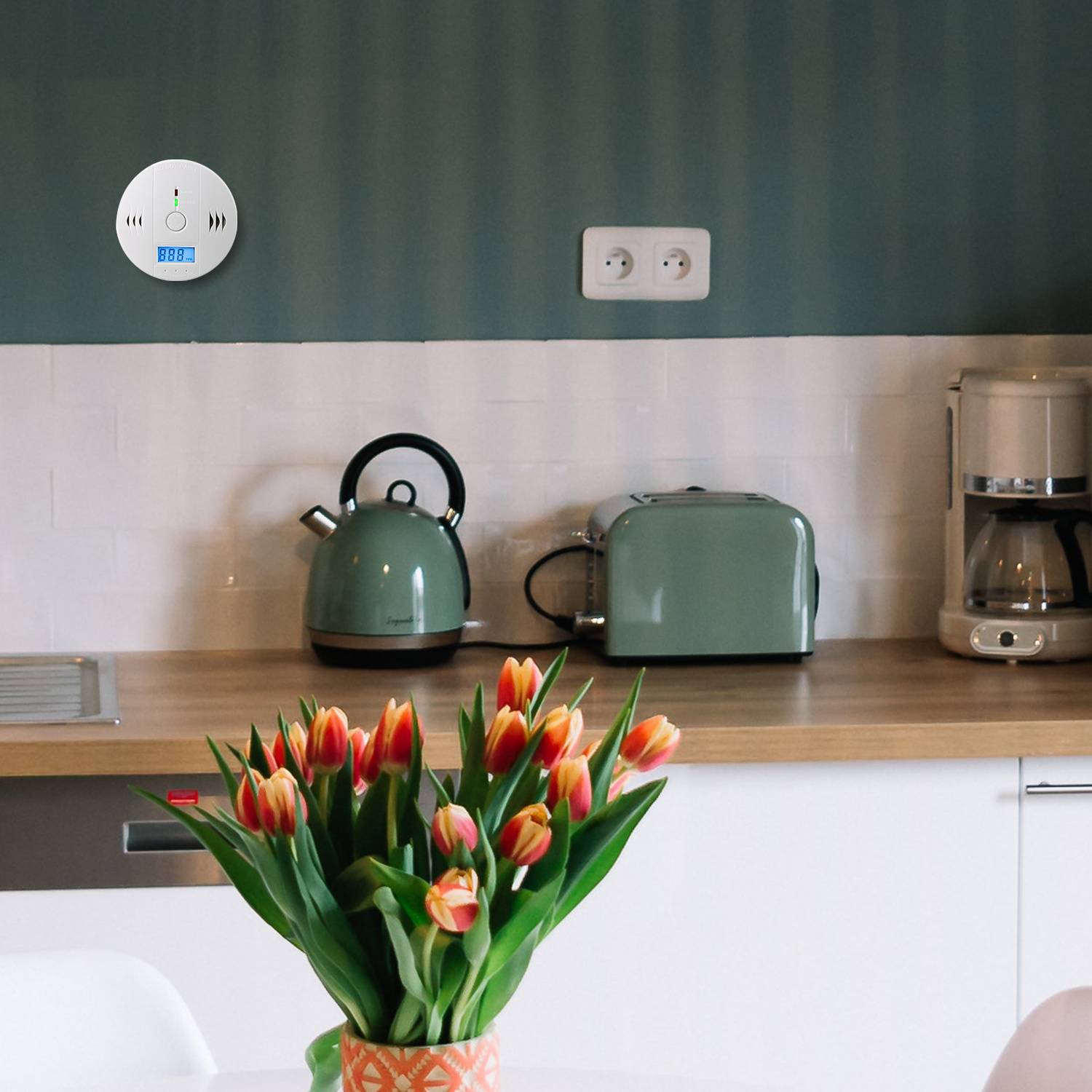 Küchentheke mit einer Vase voller rot- und gelbfarbiger Tulpen vor einem Wasserkocher, Toaster und einer Kaffeemaschine auf einer Holzarbeitsfläche.