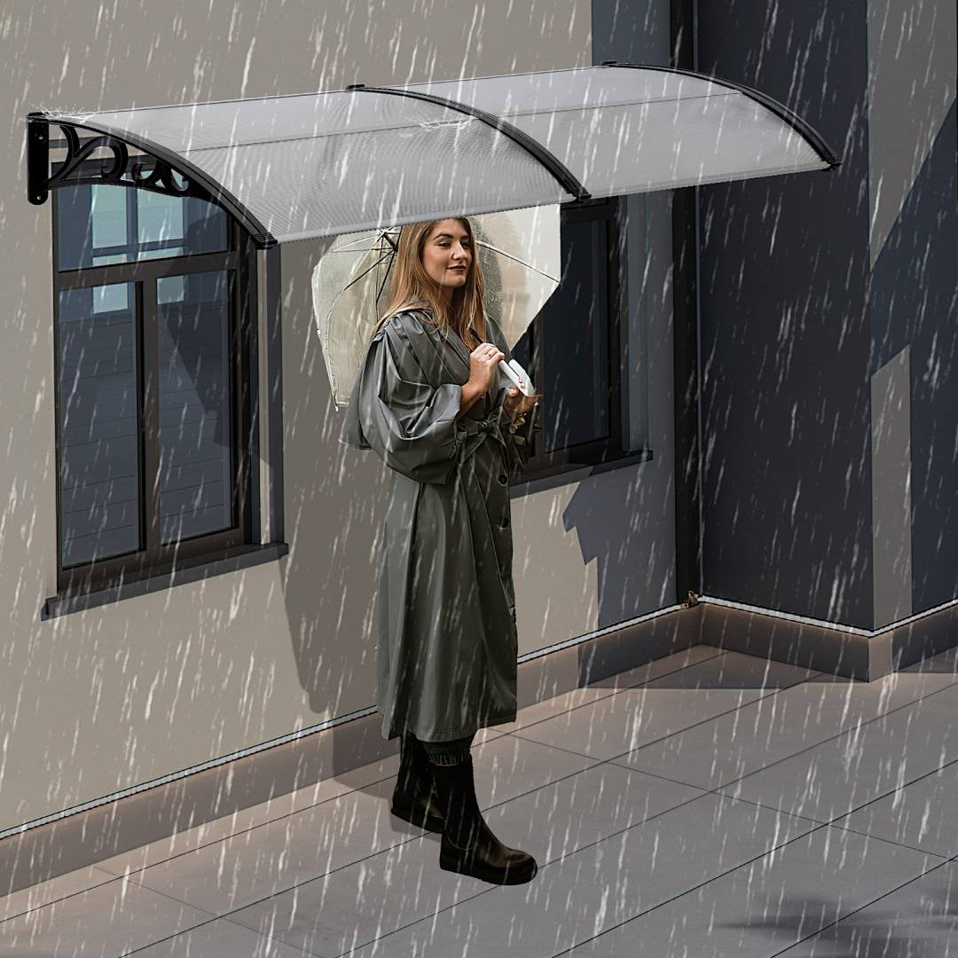 Eine Frau in einem Regenmantel steht unter einem durchsichtigen Regenschirm neben einem Gebäude, umgeben von starkem Regen.