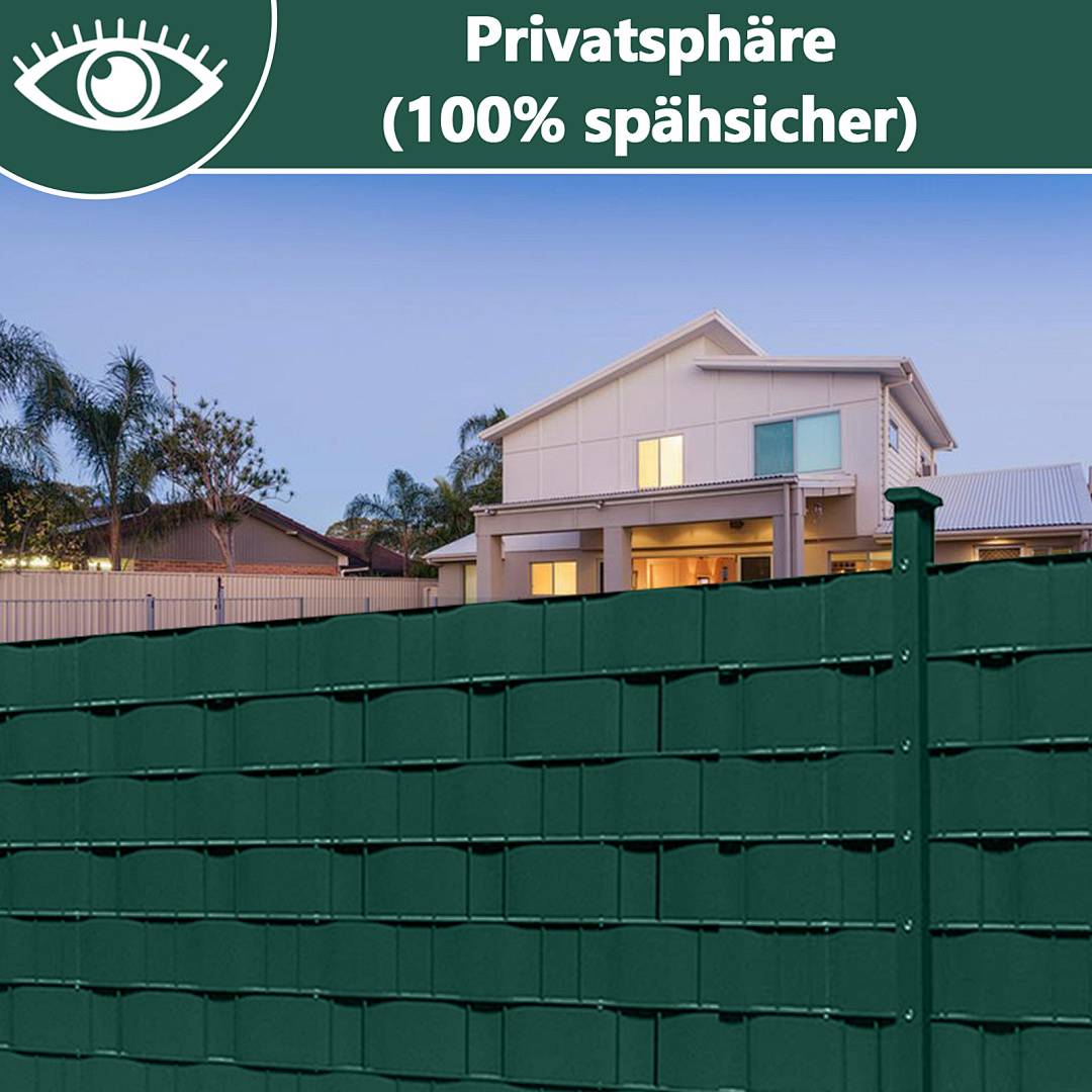 Grüner Sichtschutzzaun vor einem Einfamilienhaus in einem Wohngebiet in der Dämmerung, beschriftet mit „Privatsphäre (100% spähsicher)" mit einem Augensymbol.