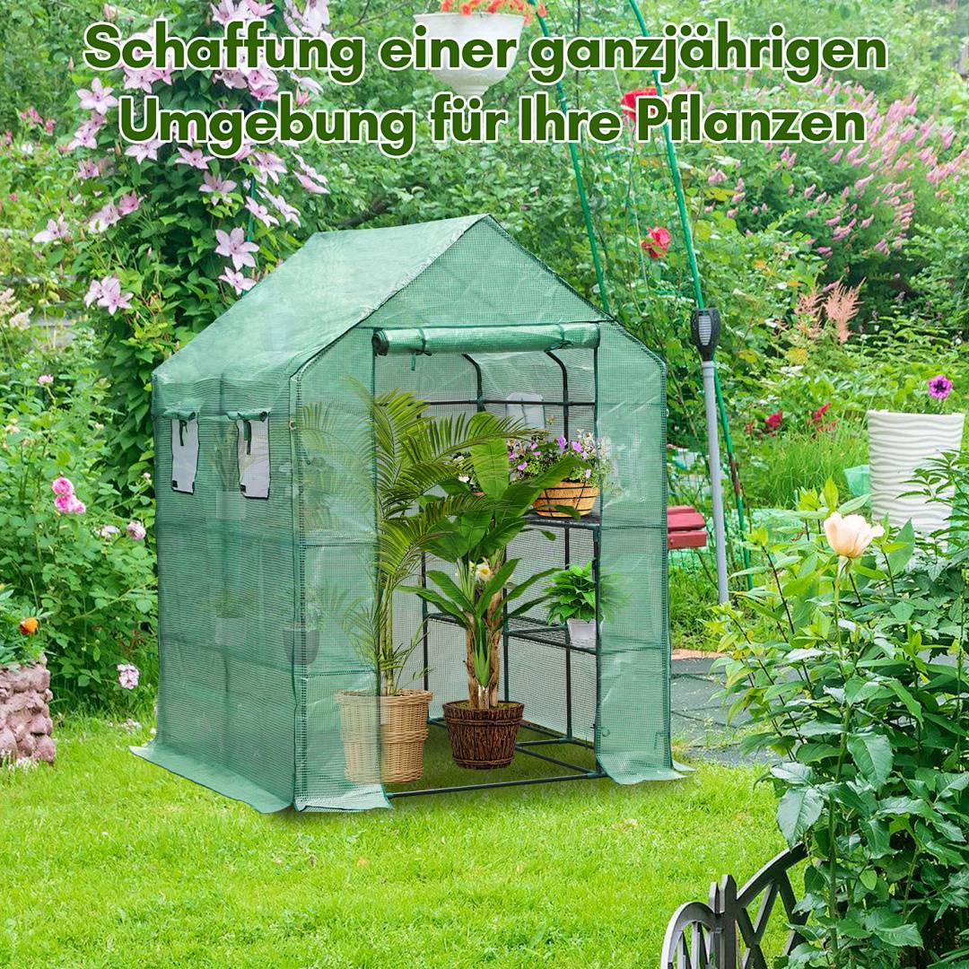 Grünes tragbares Mini-Gewächshaus in einem Garten, mit Topfpflanzen im Inneren und deutschem Text „Schaffung einer ganzjährigen Umgebung für Ihre Pflanzen" (Schaffen Sie eine ganzjährige Umgebung für Ihre Pflanzen).