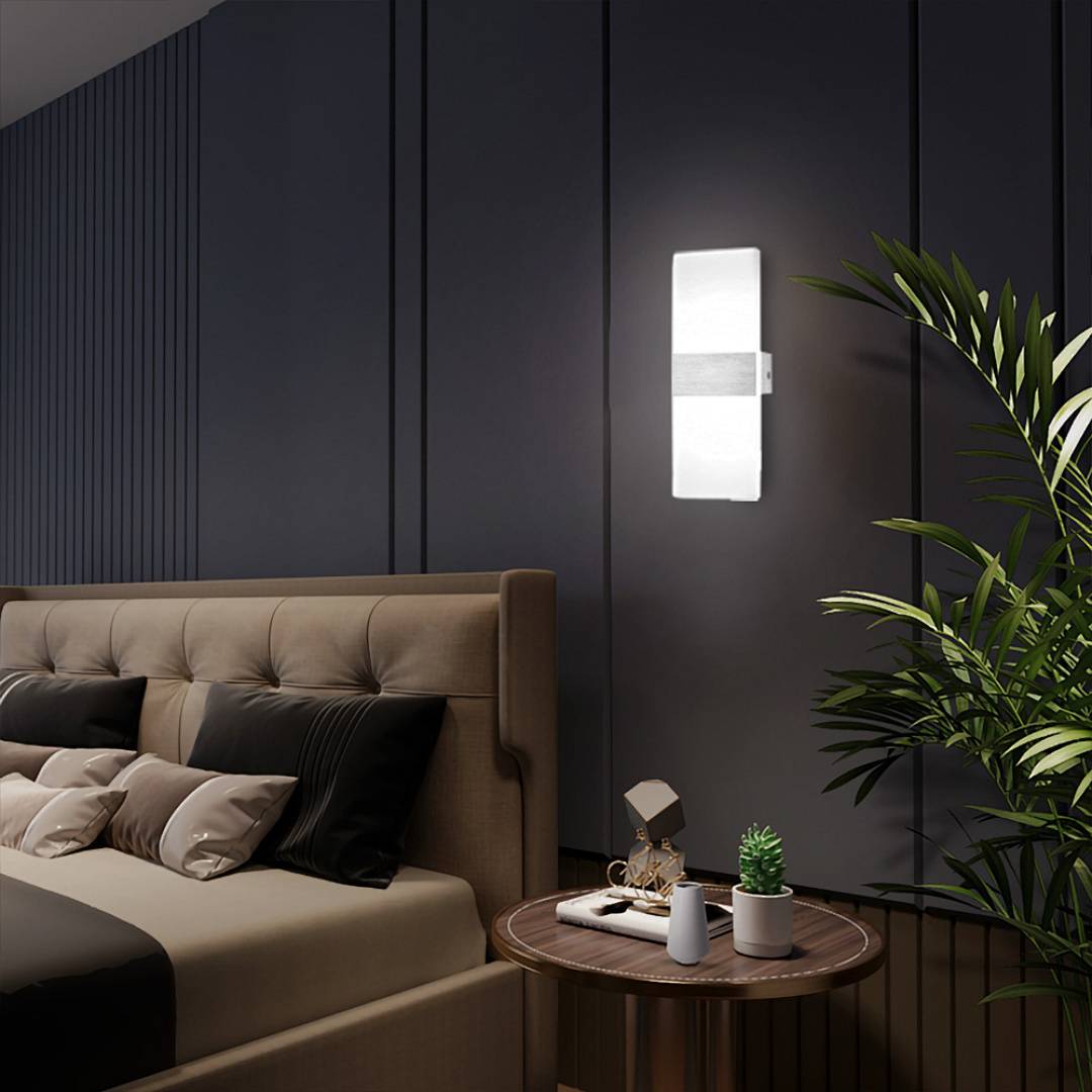 Modernes Schlafzimmer mit beigem Polsterbett, dunkler Wandverkleidung, Wandleuchte, Nachttisch und Topfpflanze.