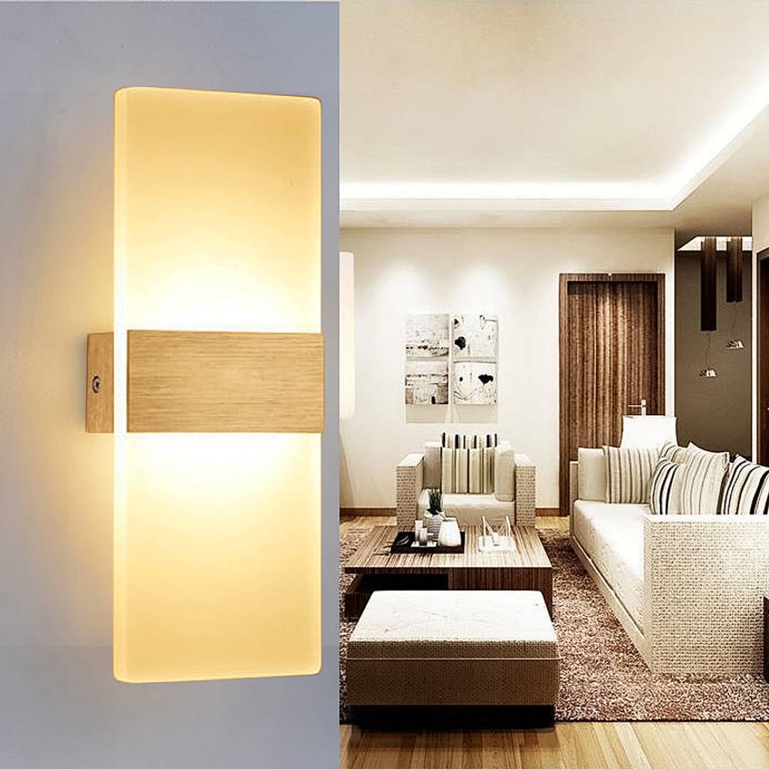 Moderne Wandleuchte mit Milchglas und Holzakzent neben einem sanft beleuchteten Wohnzimmer mit Sofa, Sessel, Fußhocker und Couchtisch.