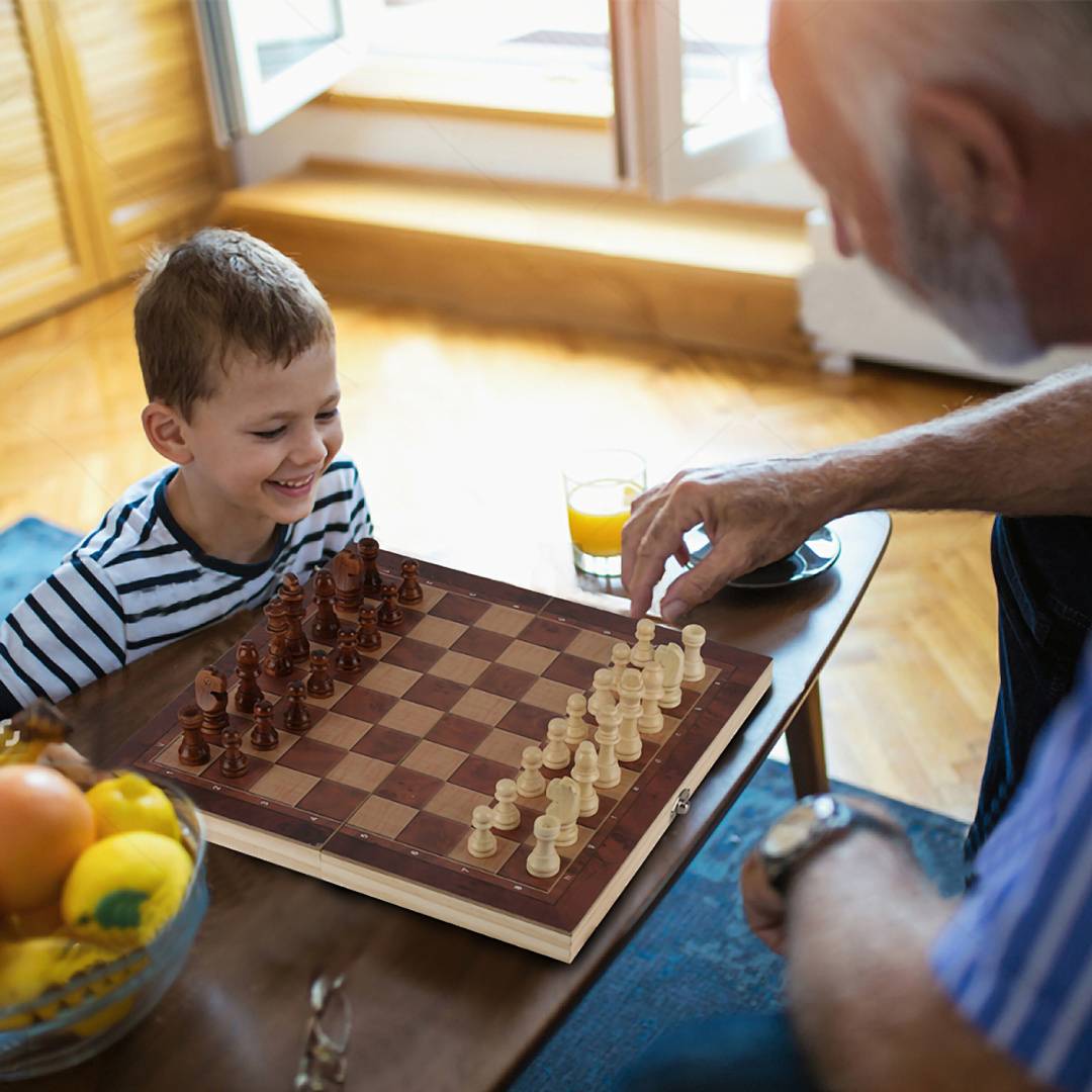 Junge und älterer Mann spielen Schach an einem Tisch, wobei der Mann ein weißes Baumaterial bewegt, während der Junge lächelt.