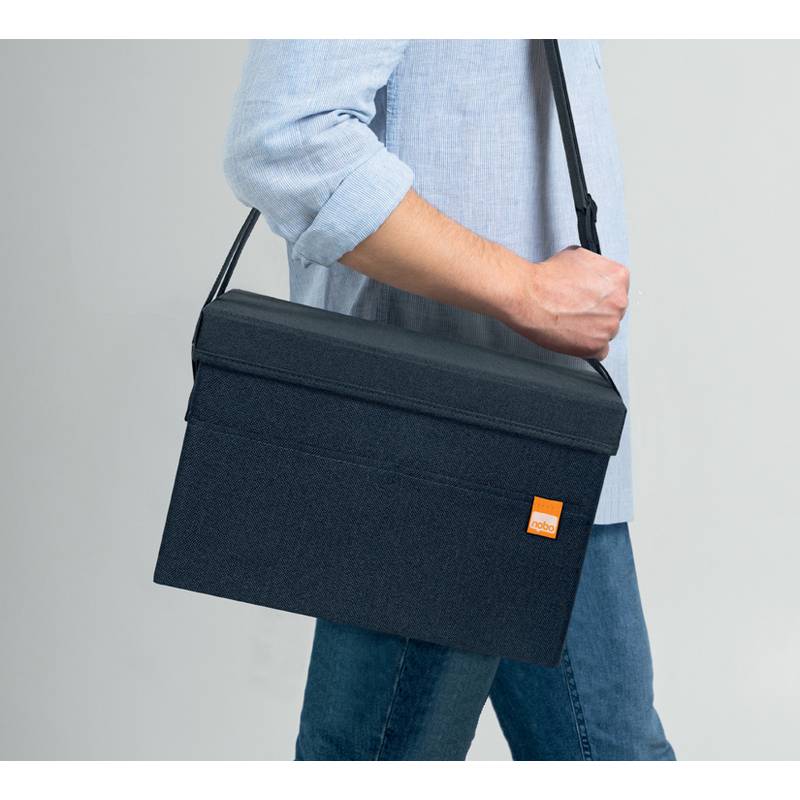 Eine Person trägt ein hellblaues Hemd und Jeans und hat eine dunkelblaue Umhängetasche mit einem orangefarbenen Anhänger, was einen lässigen, unterwegs-Stil vermuten lässt.