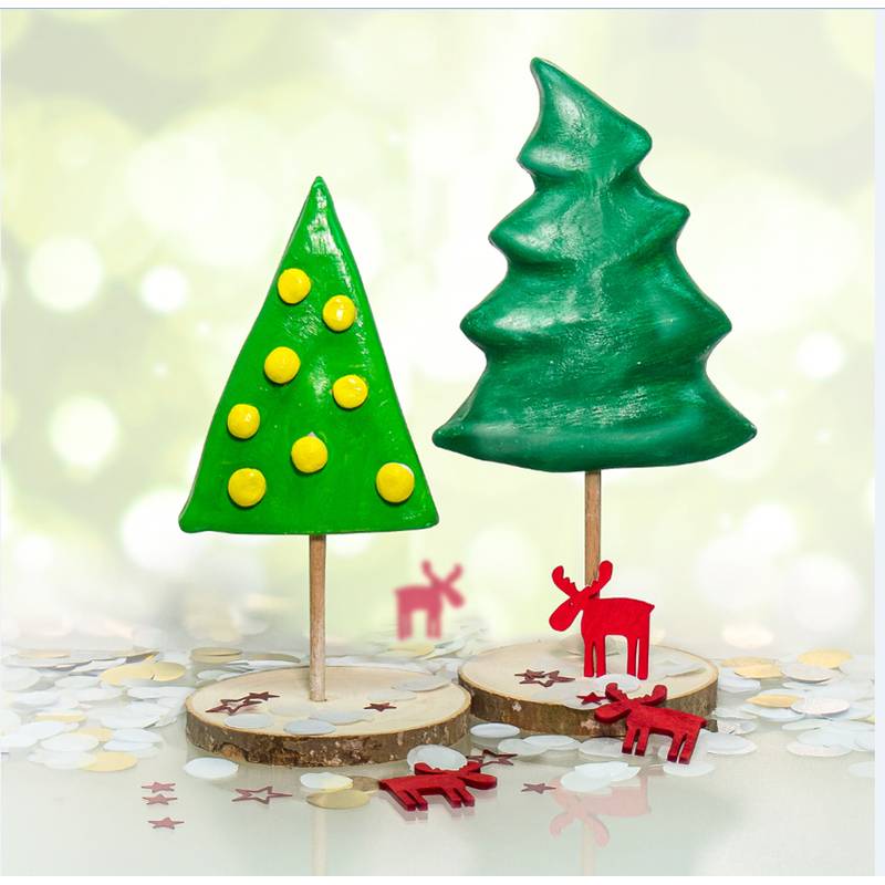 Zwei Cake Pops in Form von Weihnachtsbäumen stehen auf Holzsockeln. Der linke hat eine dreieckige Form mit gelben Punkten; der rechte ist naturalistischer gestaltet. Rote Rentierstatuen akzentuieren die Szene.