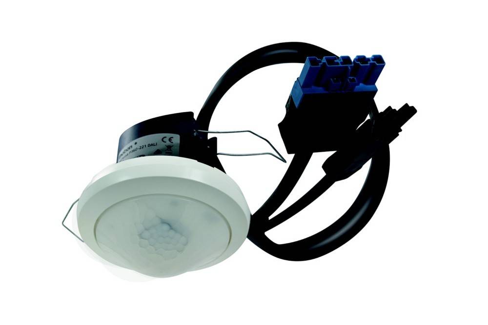 Deckenmontierter Bewegungssensor mit weißer Rundabdeckung und schwarzen Kabeln, die an einen blauen Klemmenblock angeschlossen sind, verwendet für automatische Beleuchtungssteuerung.