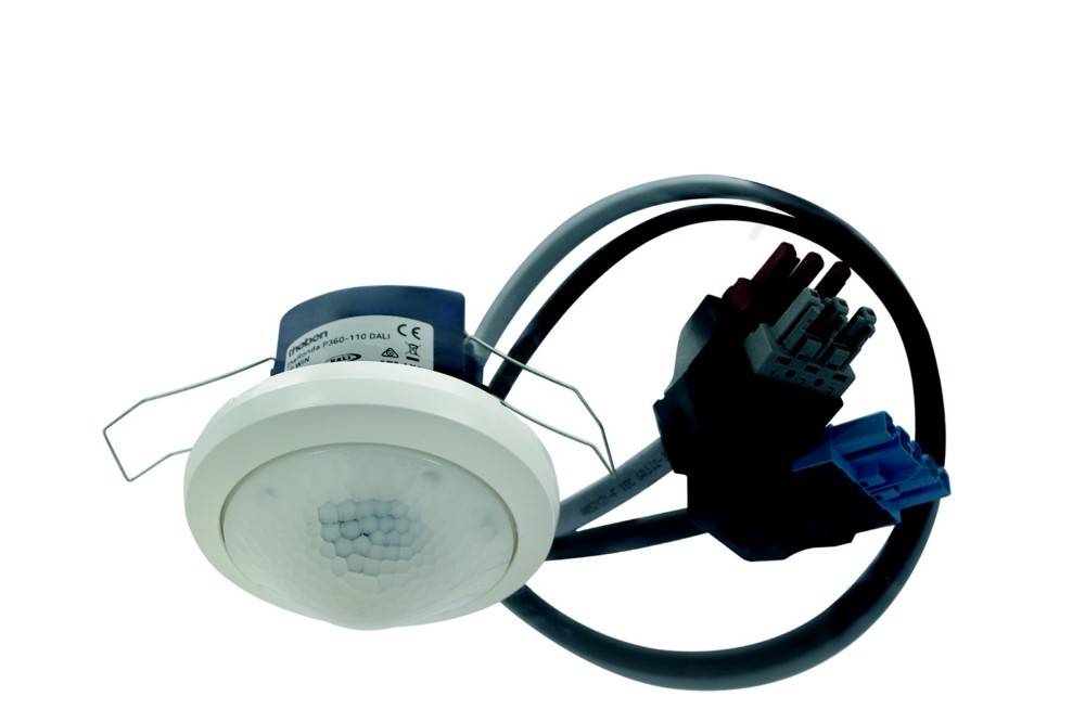 Ein kuppelförmiger elektronischer Sensor mit Verkabelung und Anschlüssen, möglicherweise ein Bewegungsmelder oder Lichtsensor, wahrscheinlich für Gebäudeautomation verwendet.