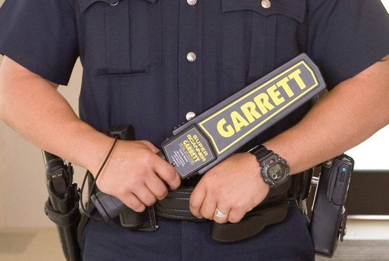 Polizeibeamter hält ein tragbares Metalldetektorgerat mit der Aufschrift „GARRETT