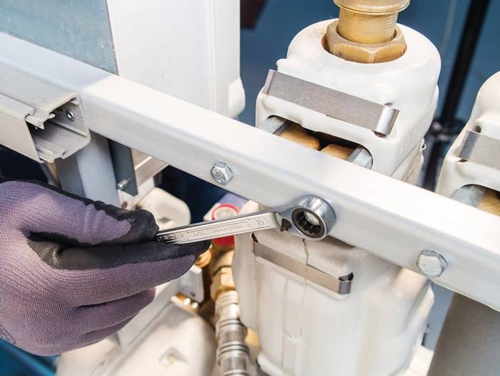 Eine Person mit Handschuhen verwendet einen Schraubenschlüssel, um einen Bolzen an einer industriellen Maschine zu befestigen und konzentriert sich dabei auf Wartungs- oder Reparaturarbeiten.