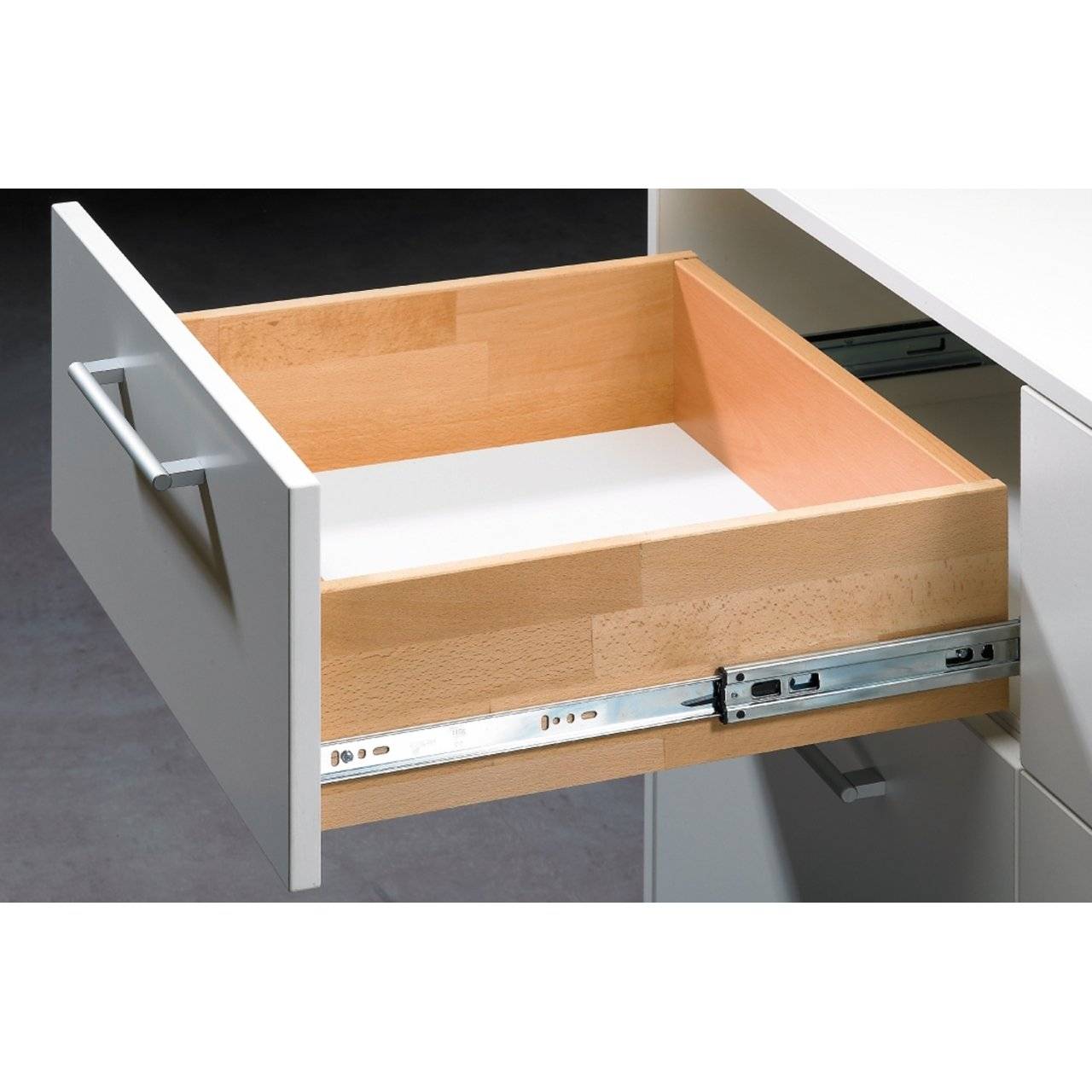 Offene Küchenlade mit hellem Holzinnere und Metallschienen, aus einem weißen Schrank herausgezogen.