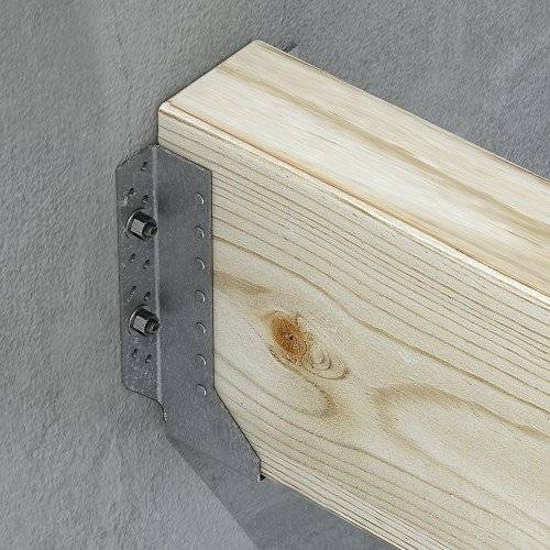 Ein Stück hellhölzernes Holz, das mit einer Metallklammer und Schrauben an einer Betonwand befestigt ist, zeigt ein Konstruktionsdetail.