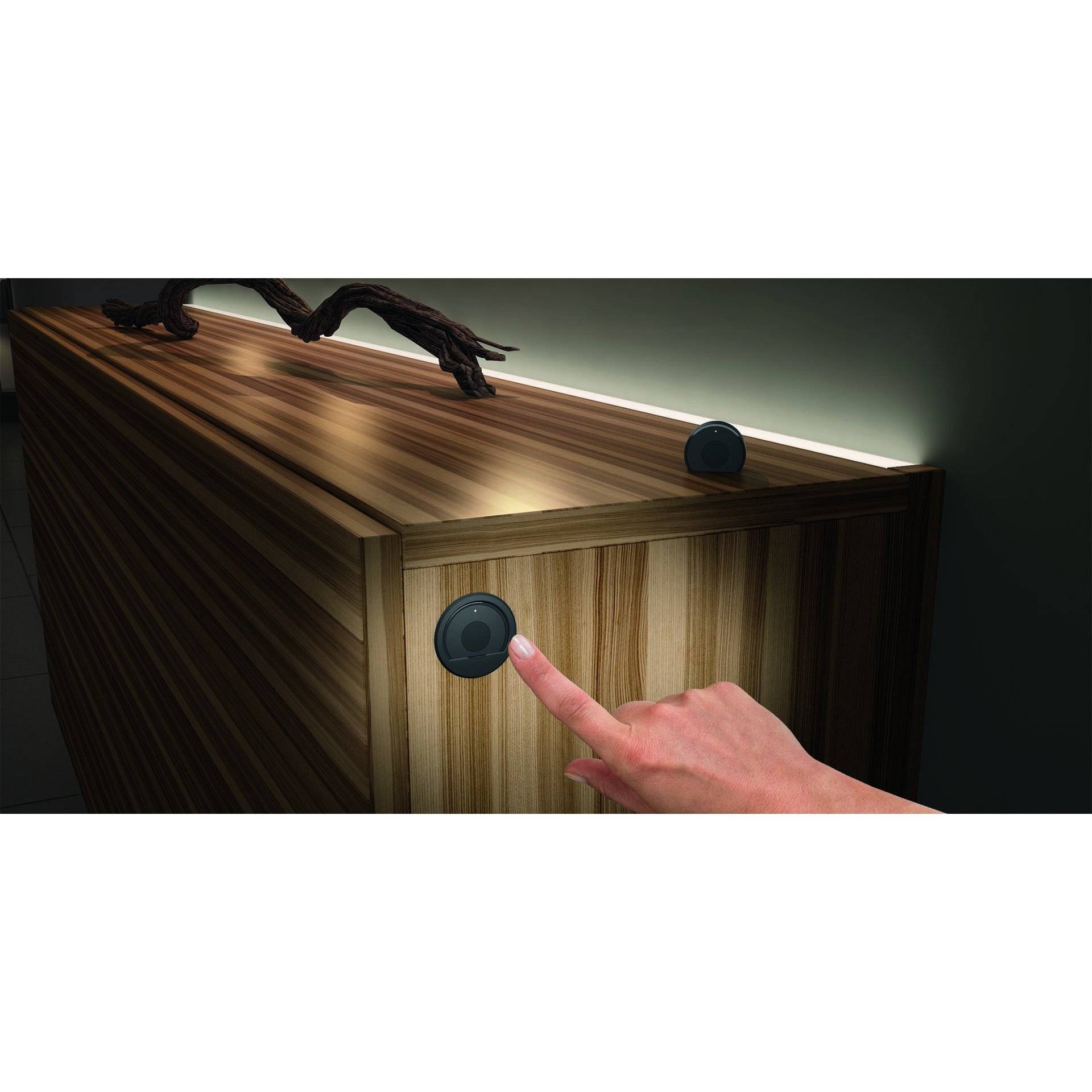 Eine Hand drückt einen runden Knopf an einem Holzschrank mit eleganter Beleuchtung, die moderne Technologie für die Möbelinteraktion hervorhebt.