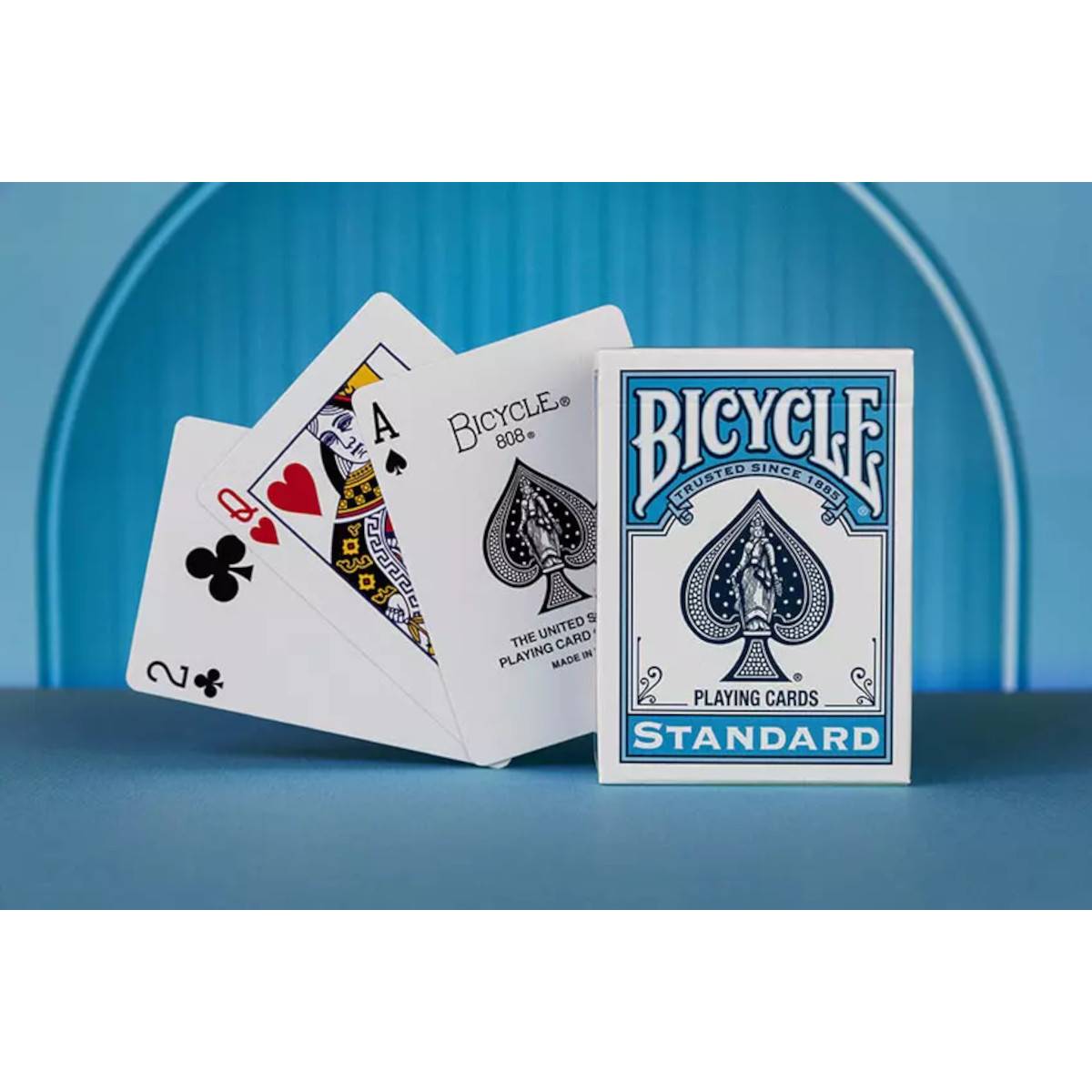 Bicycle Standard Spielkarten Schachteln neben einer fächerförmig aufgefächerten Kartenhand, die Kreuz, Herzen, Pik und Bildkarten auf blauem Hintergrund zeigt.