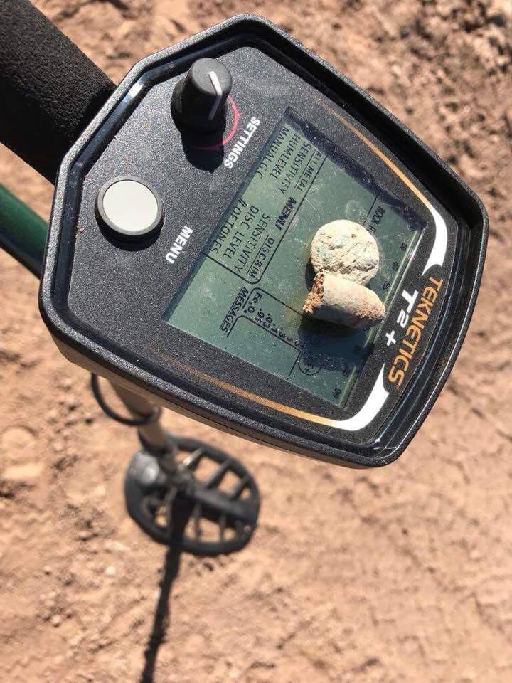 Tragbarer Teknetics T2 Metalldetektor zeigt ein Signal auf dem Bildschirm an, mit zwei kleinen Metallobjekten auf der Bedienplatte und der Suchspule sichtbar auf dem Boden.