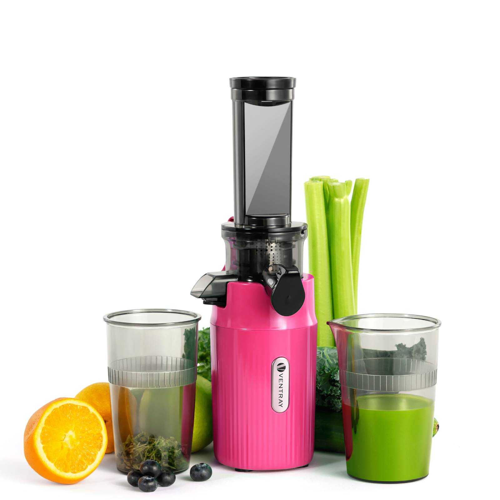 Rosa Entsafter mit zwei gefüllten Gläsern; eines mit grünem Saft, das andere mit blauem Saft und Blaubeeren. Drumherum sind Sellerie, Grünkohl und eine Orange.