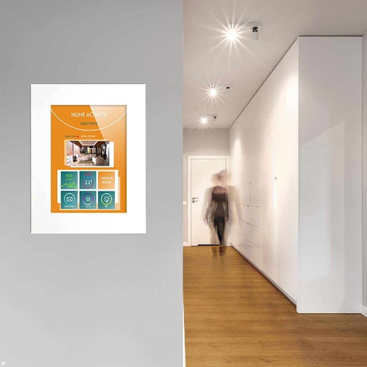 Ein Flur mit Holzböden und einer beleuchteten Decke führt zu einer verschwommenen Gestalt, die auf eine weiße Tür zugeht. Ein Poster an der Wand trägt die Aufschrift „Hausaktivität