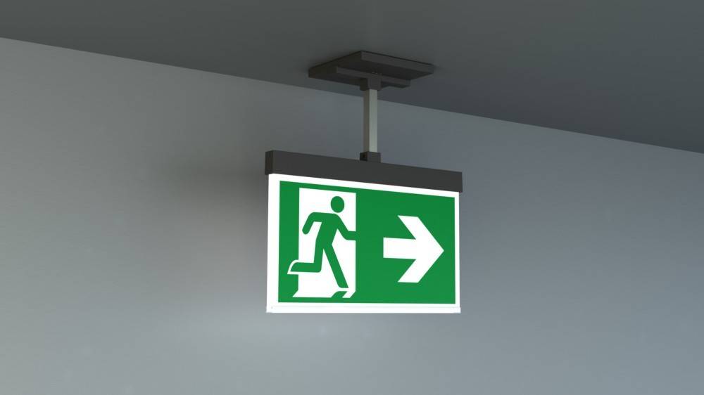 Grünes Notausgangsschild mit einer laufenden Figur und einem nach rechts weisenden Pfeil, an der Decke montiert, der die Fluchtwegrichtung anzeigt.