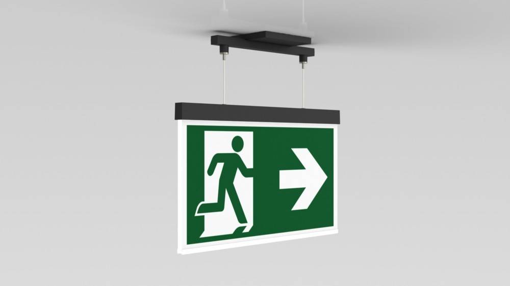 Ein Notausgangsschild von der Decke, das eine laufende Figur und einen nach rechts weisenden Pfeil zeigt, der die Richtung zum nächstgelegenen Ausgang angibt.