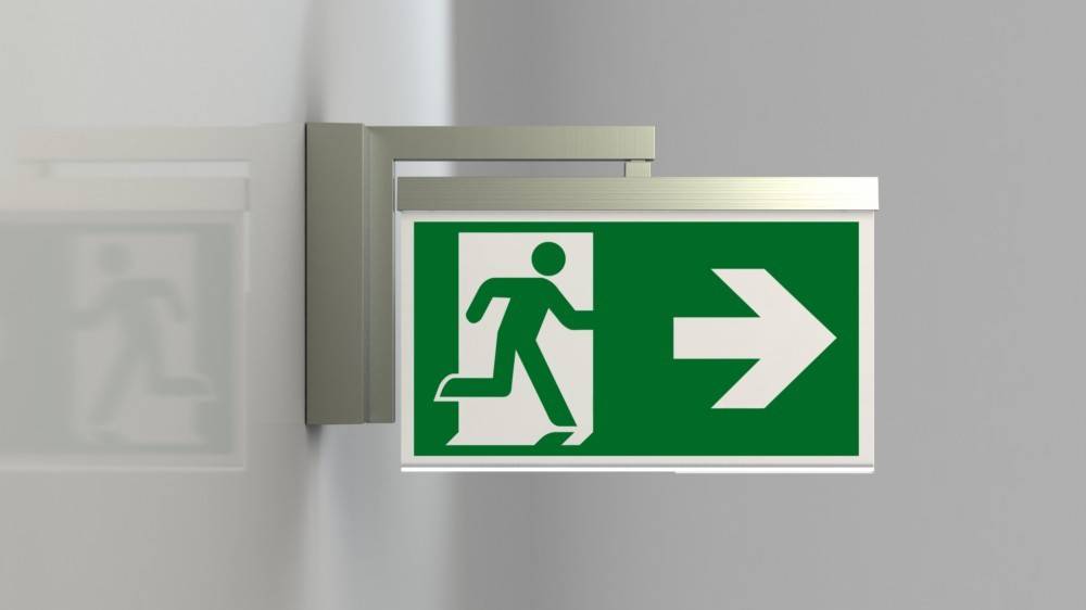 Grünes Notausgangsschild mit einer weißen laufenden Figur und einem nach rechts weisenden Pfeil, an einer Wand angebracht, der die Richtung zum Ausgang anzeigt.